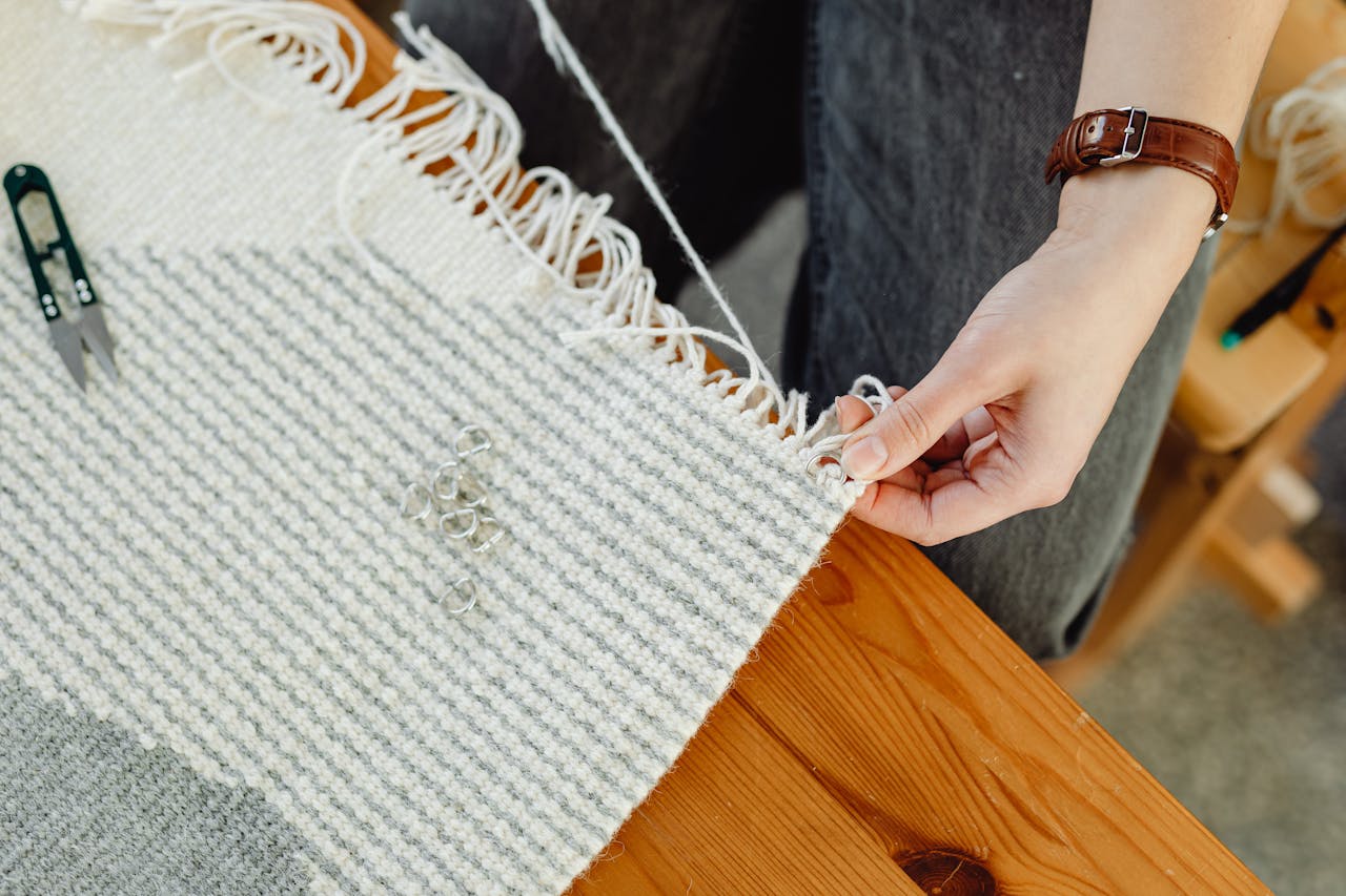 hero-img-01 Close-up of a person weaving fabric on a wooden loom, showcasing craftsmanship and detail.